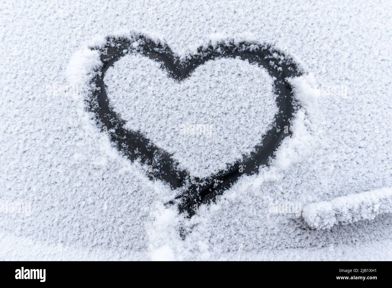 Coeur de neige sur la fenêtre de la voiture avec espace de copie. Coeur signe dans les flocons de neige frais. Symbole en forme de coeur dessiné sur le verre de voiture neigé. Concept d'amour. Saint-Valentin Banque D'Images