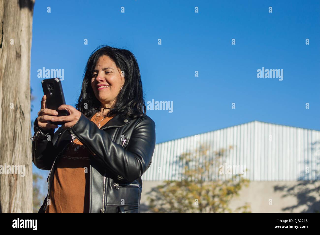 femme adulte du caucase du sud à l'extérieur d'une ferme en utilisant le téléphone souriant et communiquant avec le directeur de l'entreprise, le concept de l'industrie, l'espace de copie. Banque D'Images