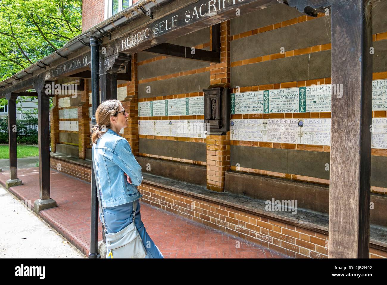 Une femme regardant les comprimés de céramique au Watts Memorial to Heroic Self-sacrifice dans Postman’s Park , Londres EC1 Banque D'Images