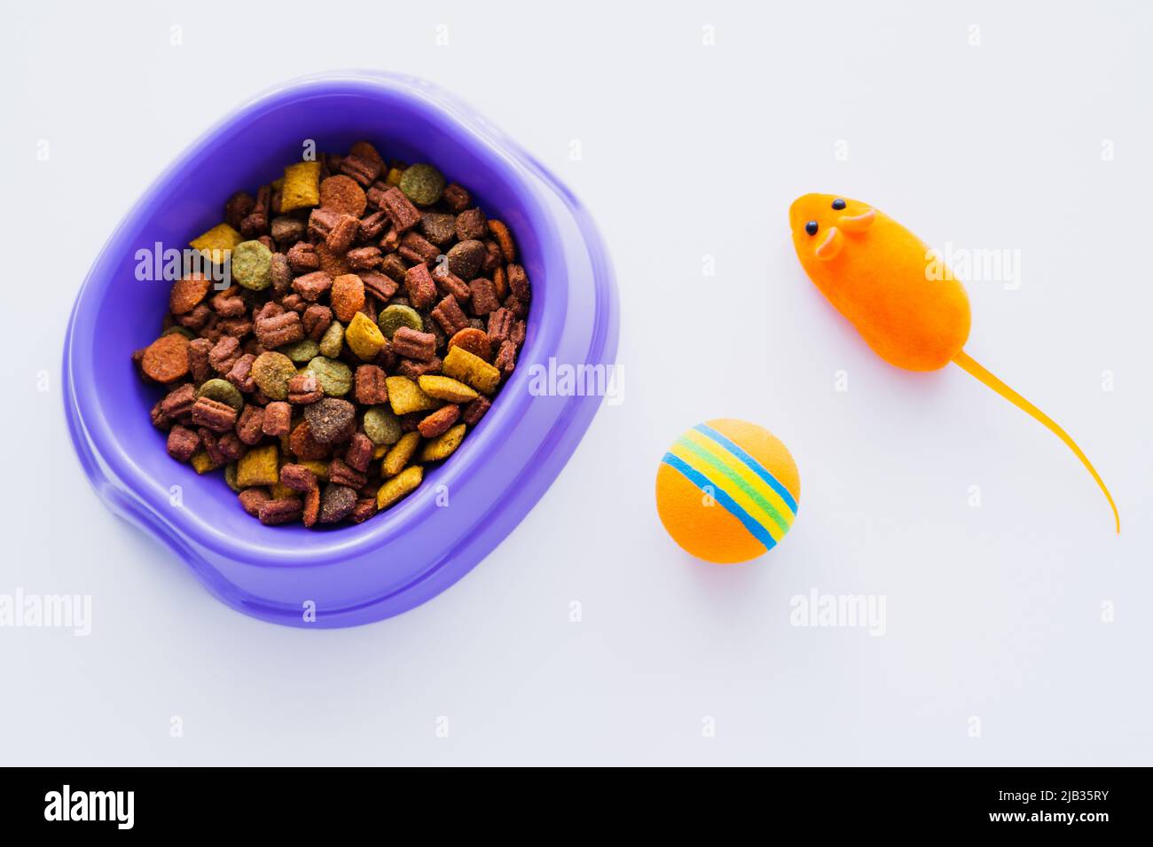 vue de dessus du bol en plastique violet avec nourriture sèche pour animaux près de la souris en caoutchouc jouet et de la balle isolée sur blanc Banque D'Images