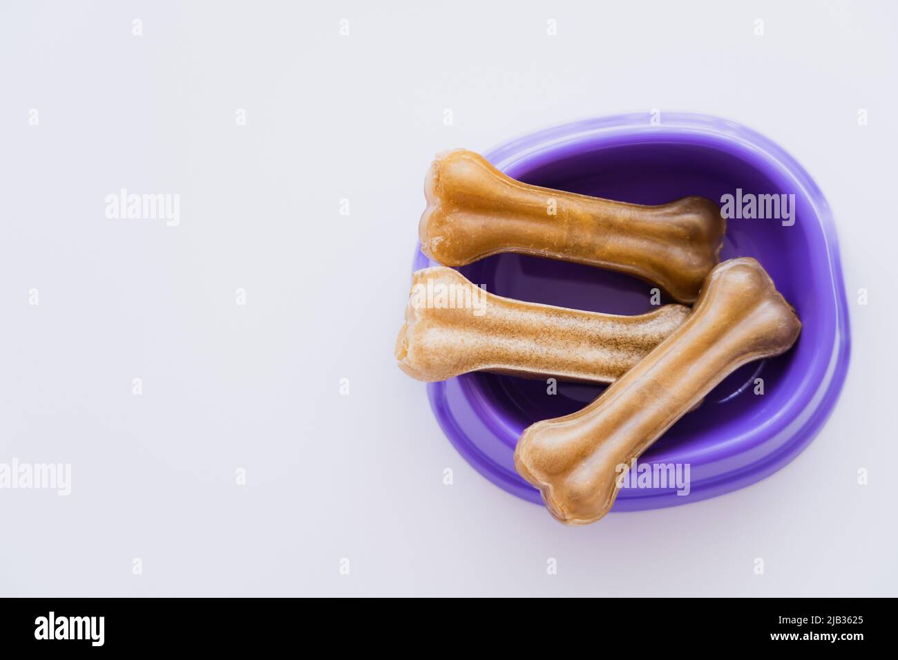 vue de dessus des friandises en forme d'os pour animaux dans un bol violet isolé sur blanc Banque D'Images