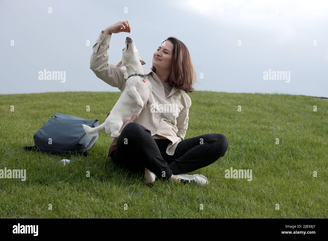 Fille donne de savoureux morceaux de gâteries pour chien à un chien blanc sur le fond du ciel Banque D'Images