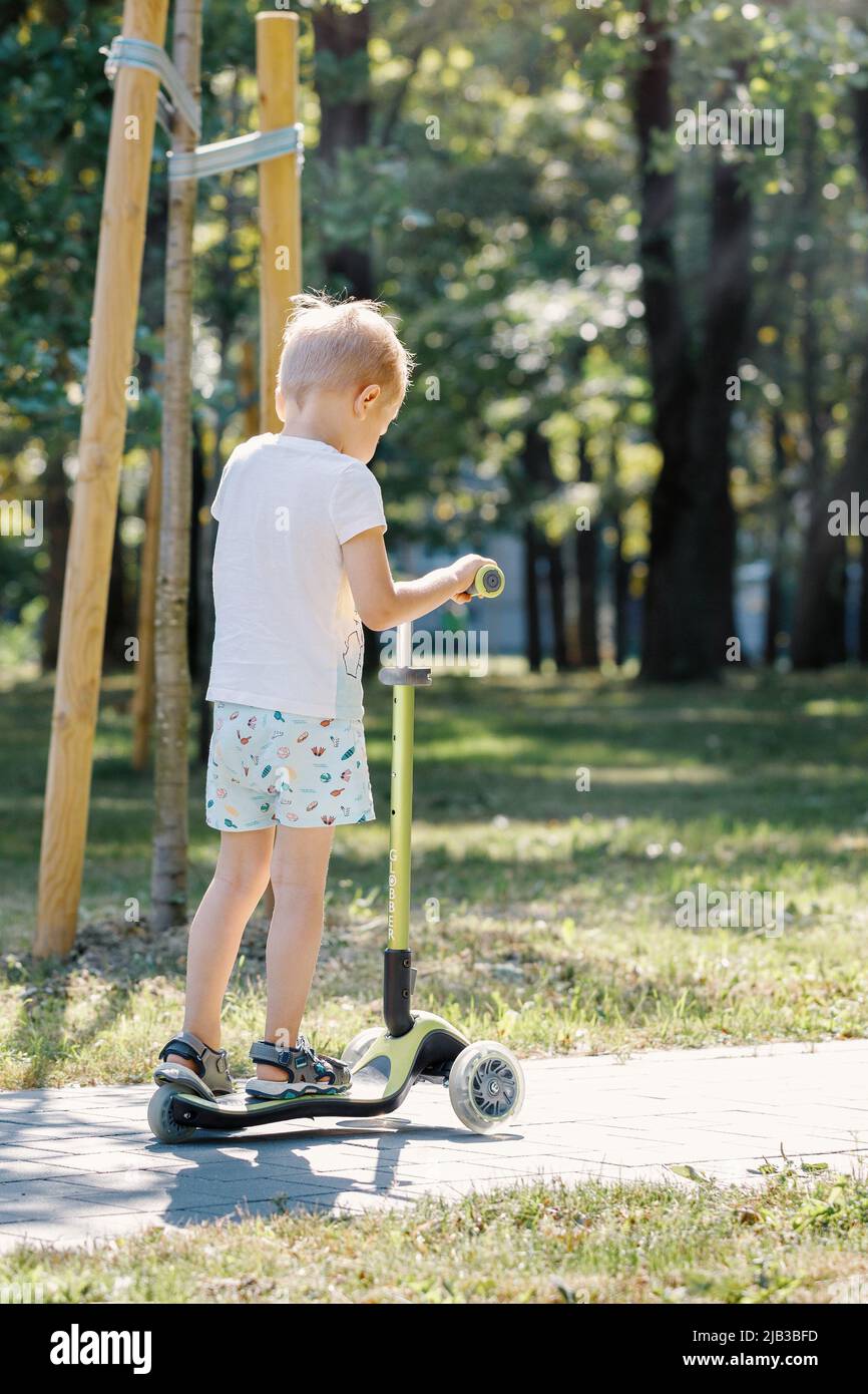 Petit garçon en scooter. Les enfants font du kick board. Enfant jouant dans la rue de banlieue par beau temps d'été. Activité de plein air saine. Mignon enfant sur son chemin Banque D'Images
