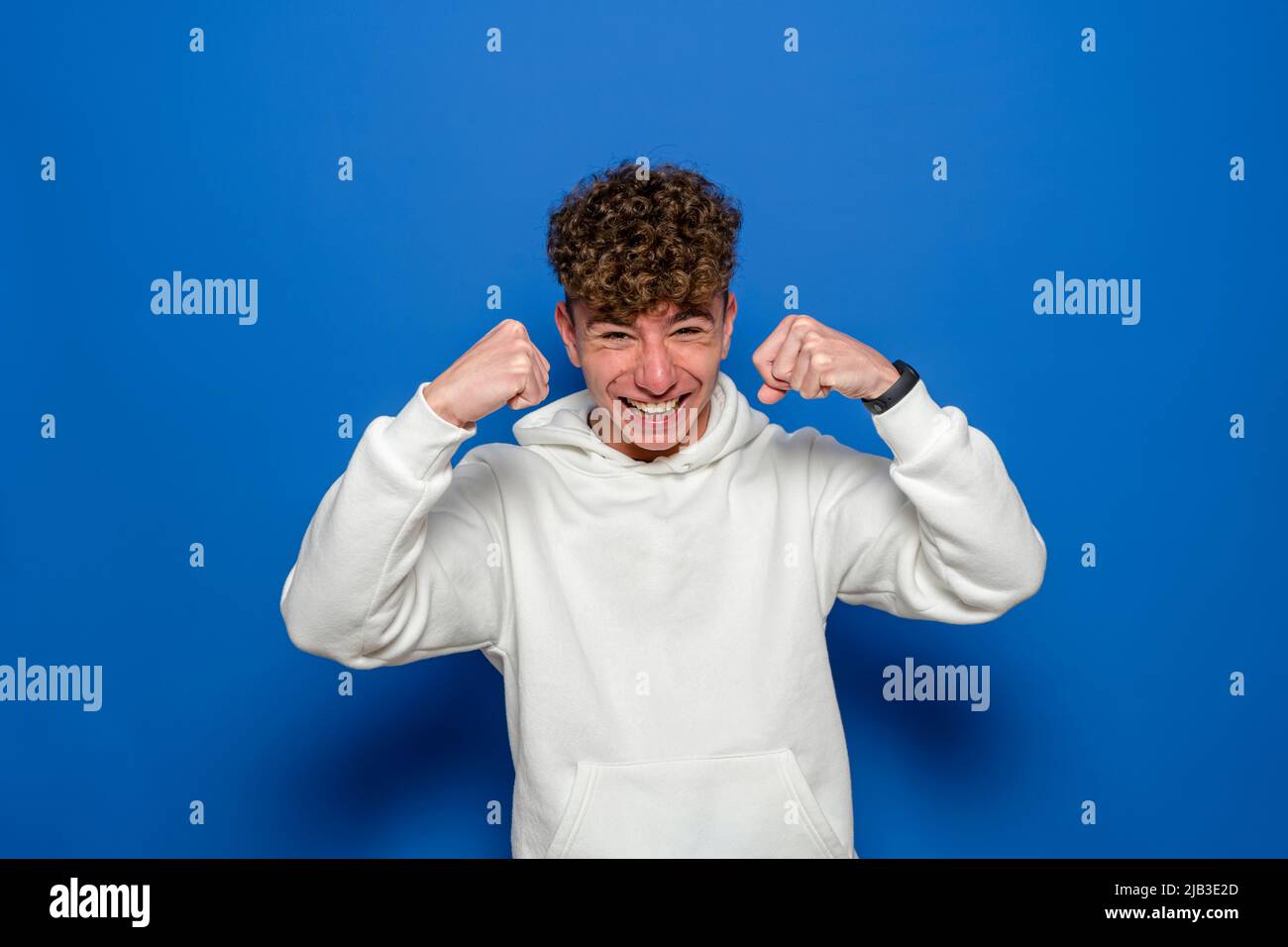 Sportif robuste choqué jeune homme 20s portant un sweat-shirt blanc debout montrant les muscles du biceps regarde la caméra isolée sur fond bleu studio Banque D'Images