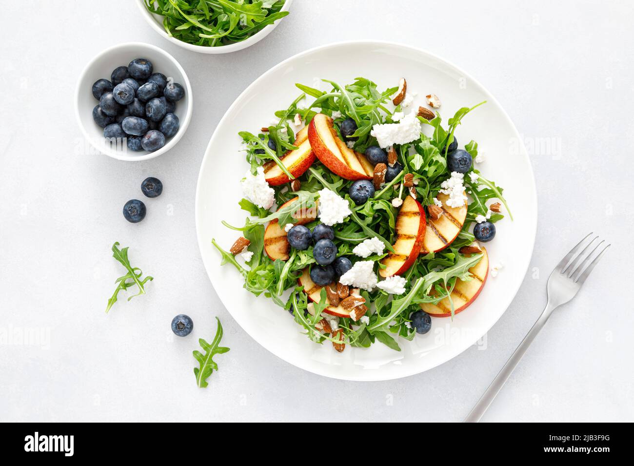 Salade de fruits frais à la pêche, aux myrtilles et aux arugula avec fromage et noix d'amande, vue du dessus Banque D'Images