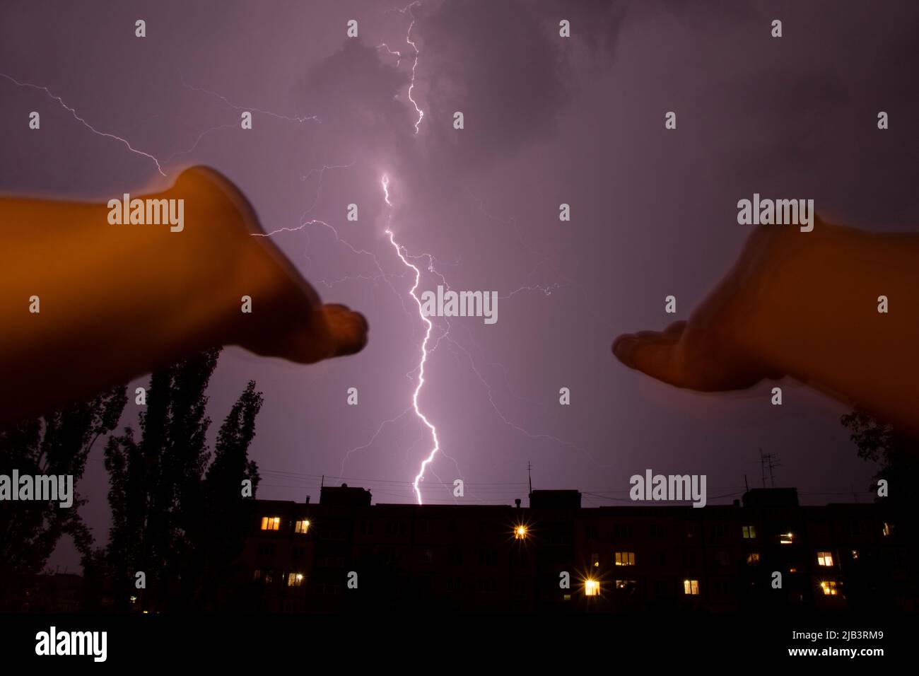 Les mains des femmes sont étirées vers le ciel sur fond de foudre au-dessus de la ville et des maisons la nuit, une prière à Dieu pendant un orage, Banque D'Images