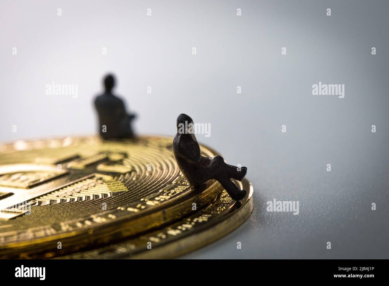 L'homme d'affaires miniature assis sur les bitcoins et appelant avec son téléphone mobile sur fond blanc Banque D'Images