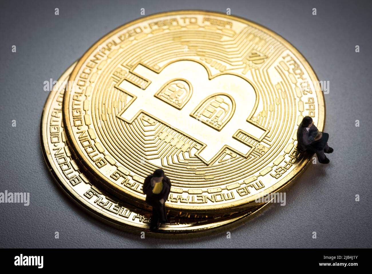 Les hommes d'affaires en miniature assis sur les bitcoins sur fond blanc de l'angle vertical dans l'humeur sombre. Banque D'Images