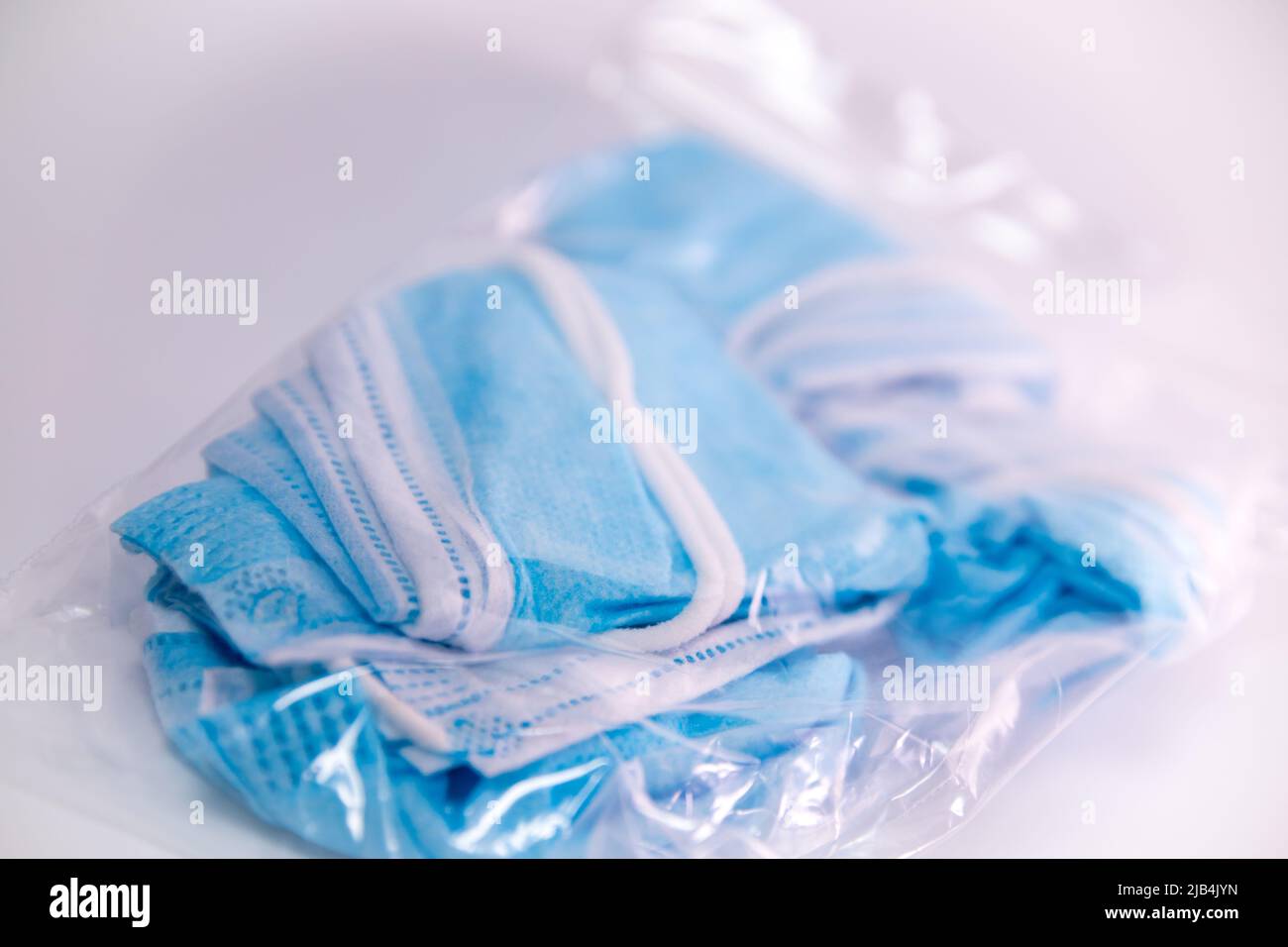 Masques faciaux bleus froissés déjà utilisés emballés dans un sac à fermeture éclair transparent sur fond blanc. Banque D'Images