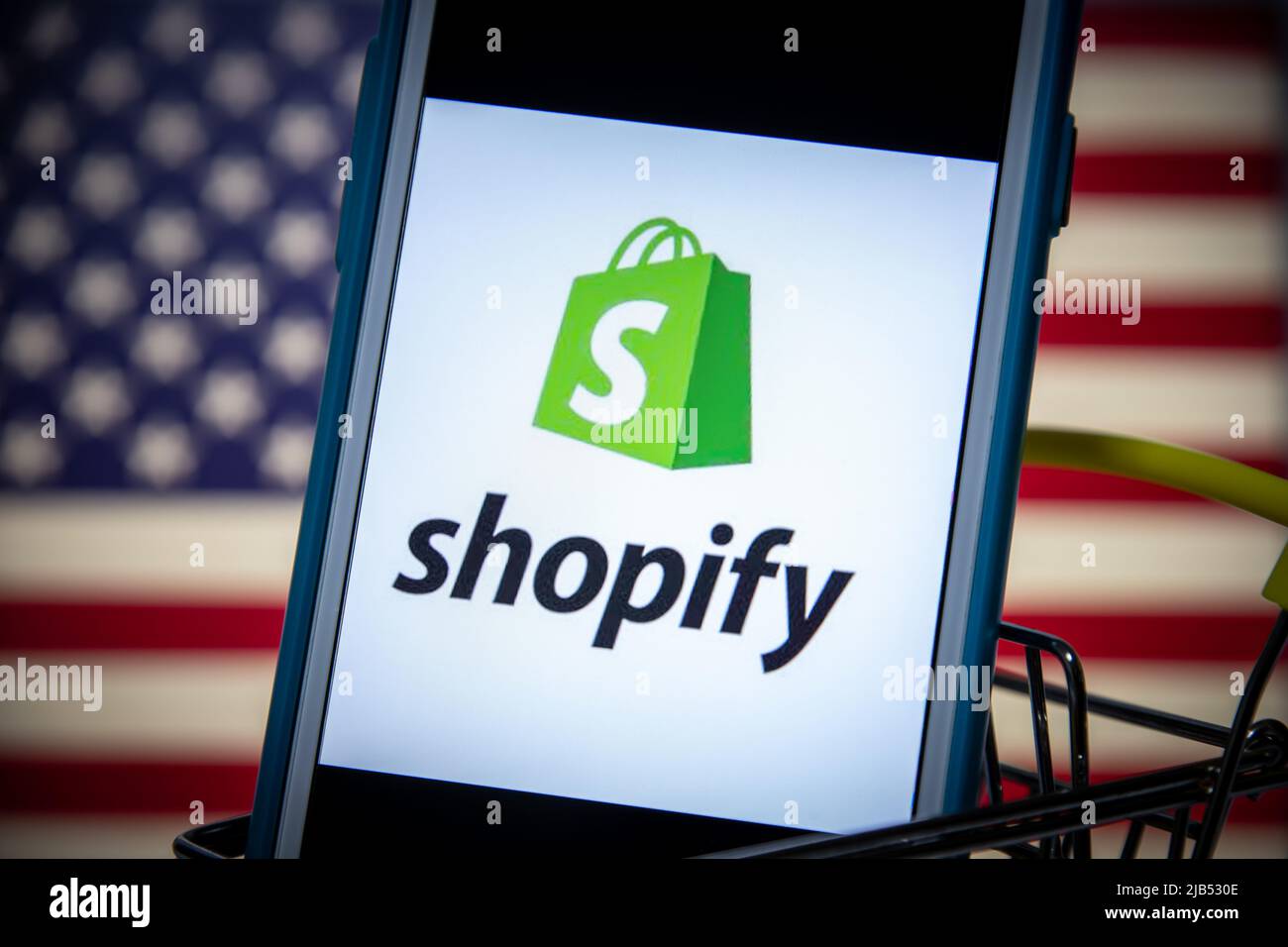 Logo de Shopify, société multinationale canadienne de commerce électronique (magasins en ligne et systèmes de point de vente au détail), sur iPhone dans un panier avec drapeau américain Banque D'Images