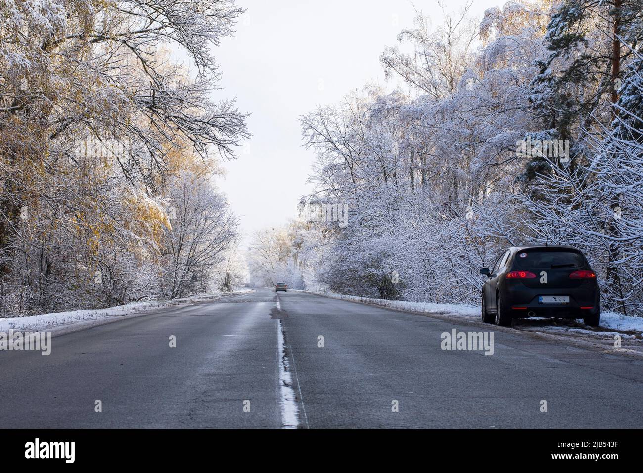La voiture se trouve sur le côté de la route sur une route enneigée dans les bois. Piste d'hiver pendant la première neige. Banque D'Images