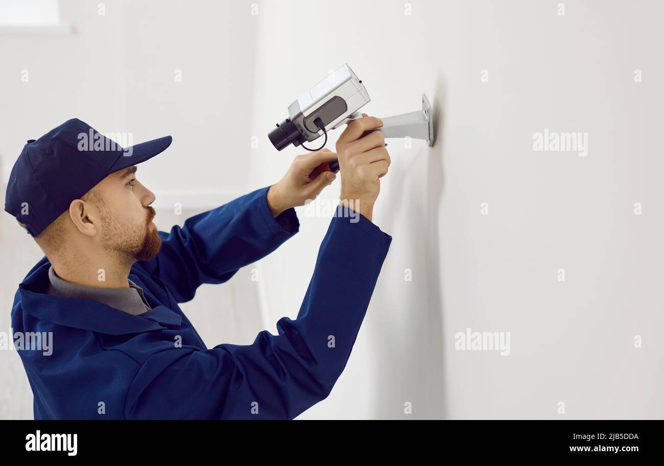 Un technicien professionnel répare ou installe un système de caméra de vidéosurveillance sur un mur à l'intérieur de la maison. Banque D'Images