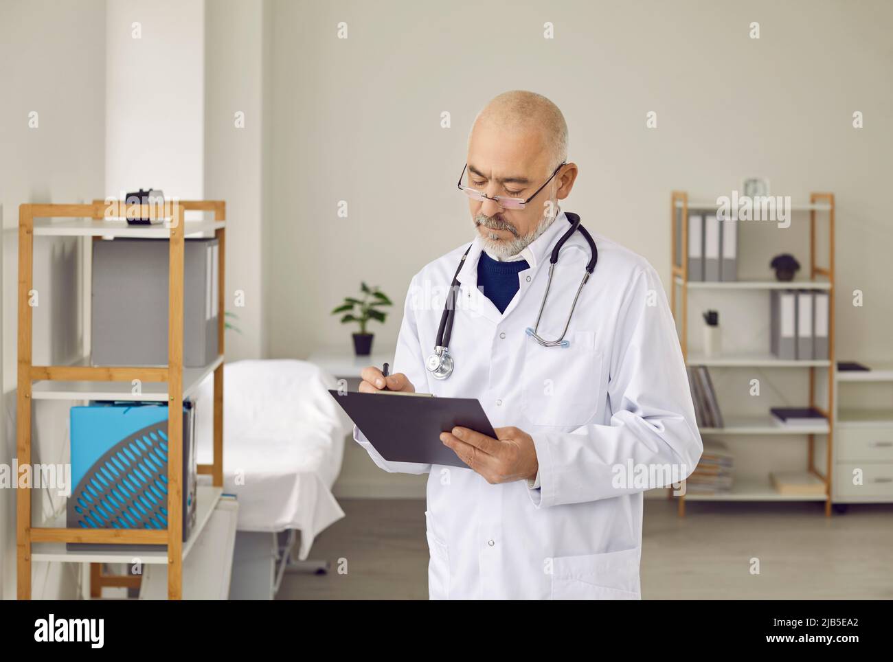 Un médecin de sexe masculin plus âgé écrit sur une carte médicale Banque D'Images