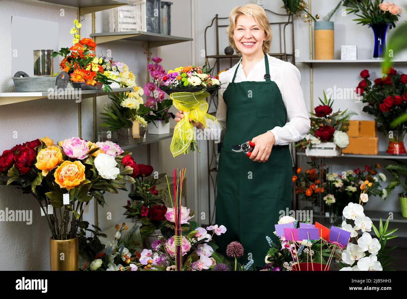 Fleuriste en tablier tenant des ciseaux et fixant des fleurs Banque D'Images
