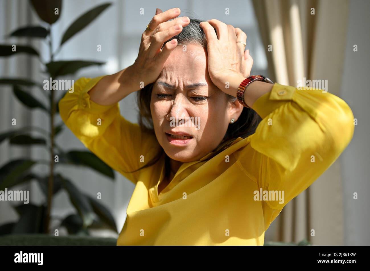 Une femme asiatique d'âge moyen mal en contact avec la tête, souffre de migraines à la maison. Malade femme âgée fatiguée ayant un problème de santé. Banque D'Images