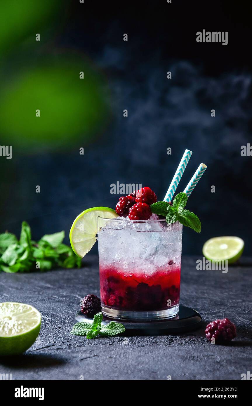 Cocktail avec rhum ou vodka, soda, purée de framboises et mûres, citron  vert et menthe dans le verre avec fumée sur fond gris foncé Photo Stock -  Alamy