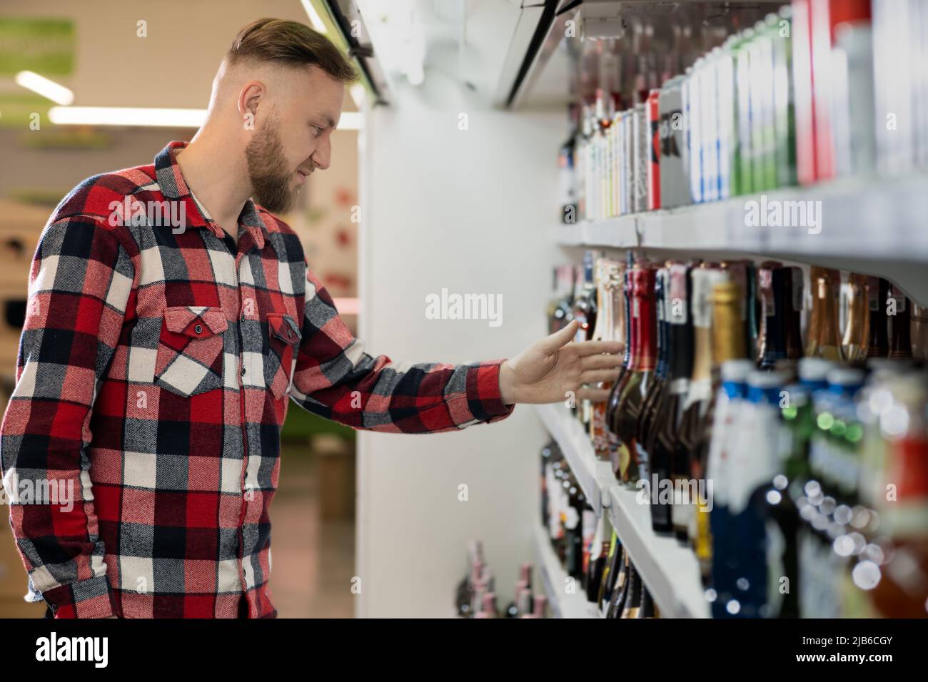 beau shopper masculin en choisissant le champagne au supermarché, un gars debout près de l'étagère avec l'alcool faible du marché du vin, vin mousseux dans l'épicerie Banque D'Images