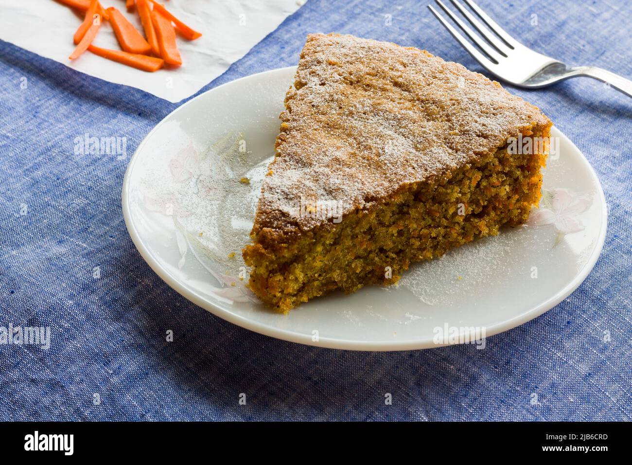 Vue rapprochée d'une tranche de gâteau frais au Carrot avec sucre glace arrosé sur le dessus, placé sur fond bleu foncé. Gâteau à thé humide, fait maison, doux d'été. Banque D'Images