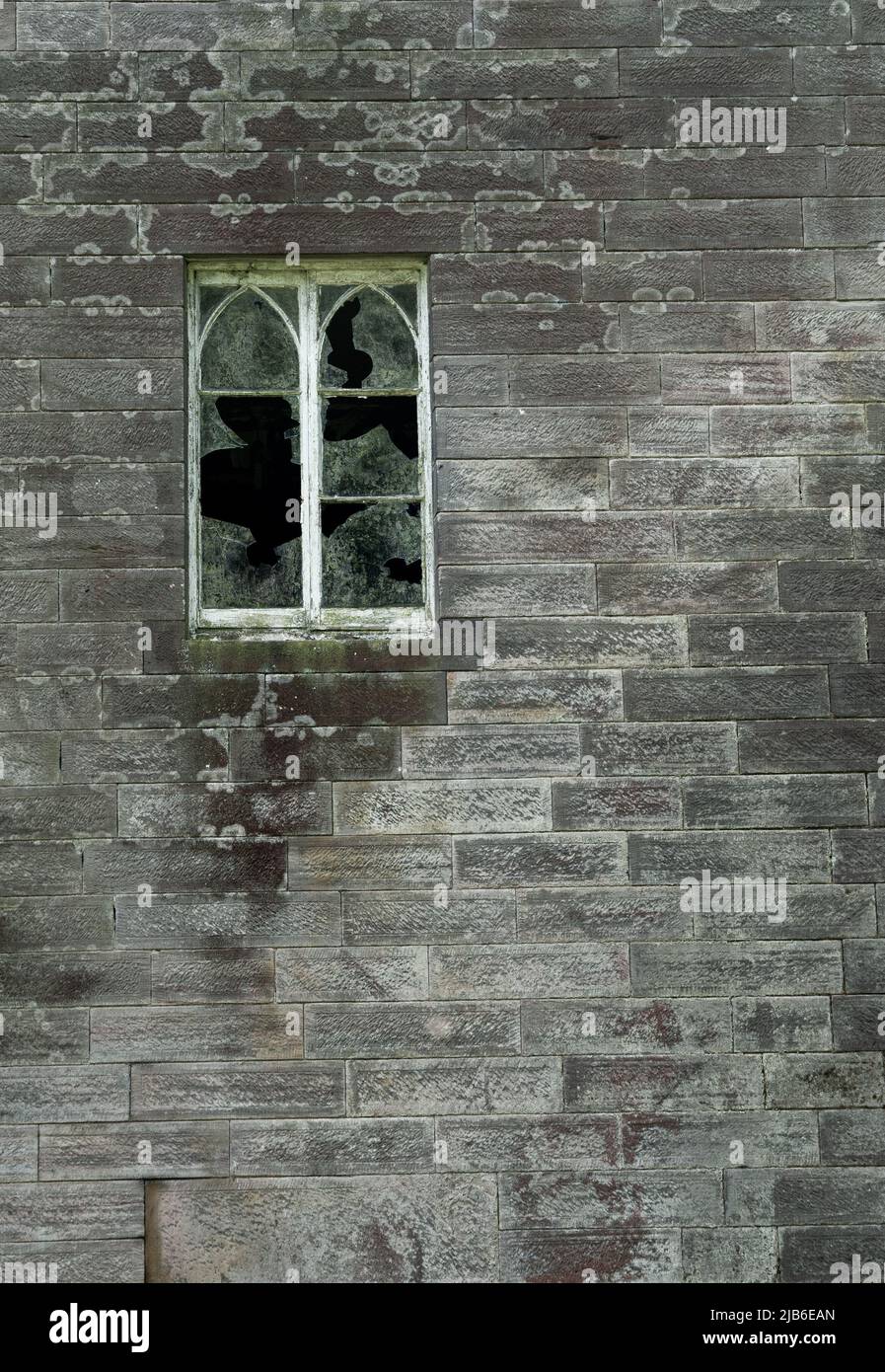 Fenêtre cassée avec verre brisé dans le mur de pierre altérée d'un bâtiment abandonné Banque D'Images