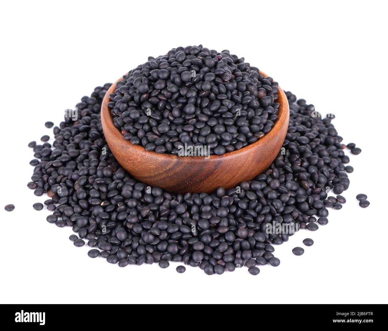 Lentilles noires dans un bol en bois, isolées sur fond blanc. Pile de grains de lentilles de béluga secs Banque D'Images