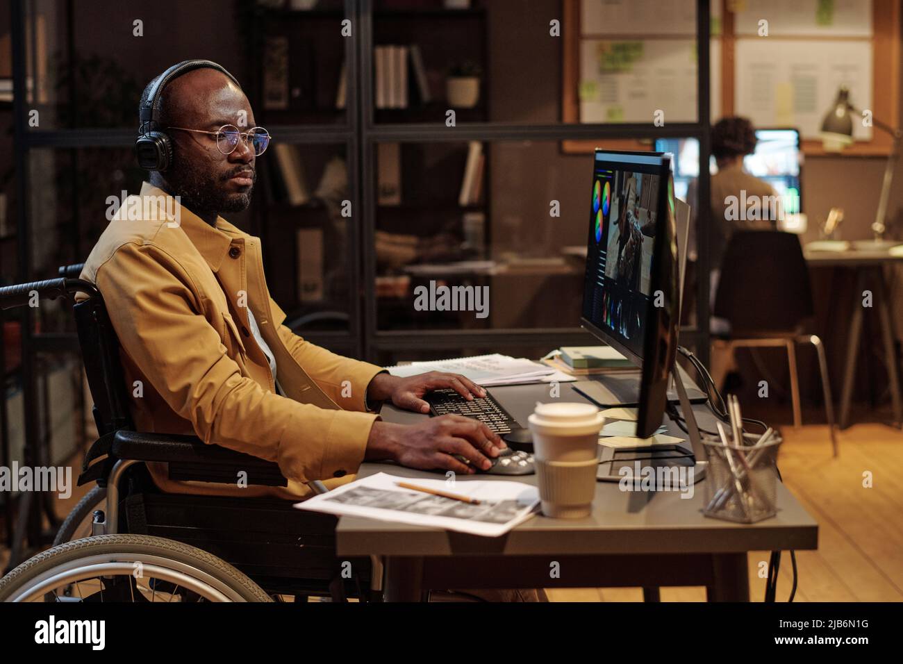 Homme africain en fauteuil roulant éditant une vidéo à l'aide d'un logiciel de post-production portant des écouteurs Banque D'Images