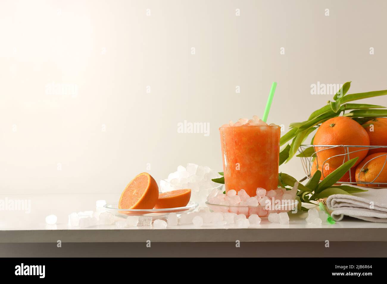 Détail de la boisson d'orange avec beaucoup de glace sur une table blanche avec des fruits et un bol avec de la glace autour et un fond isolé. Vue avant. COM. Horizontale Banque D'Images