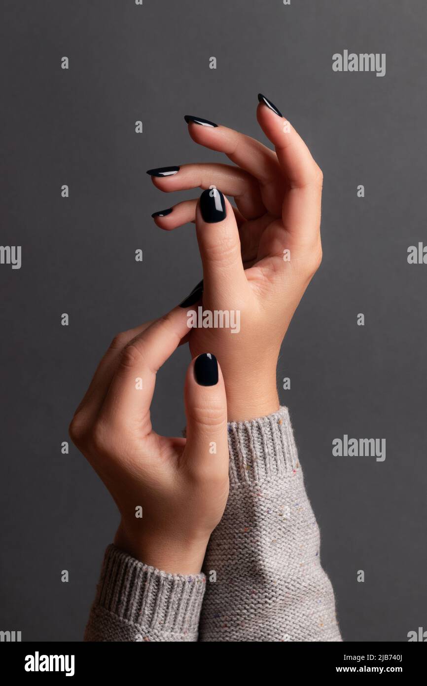 Les mains des femmes sont en tricot gris avec une belle manucure - ongles  noirs foncé sur fond gris.Concept de soin des ongles Photo Stock - Alamy