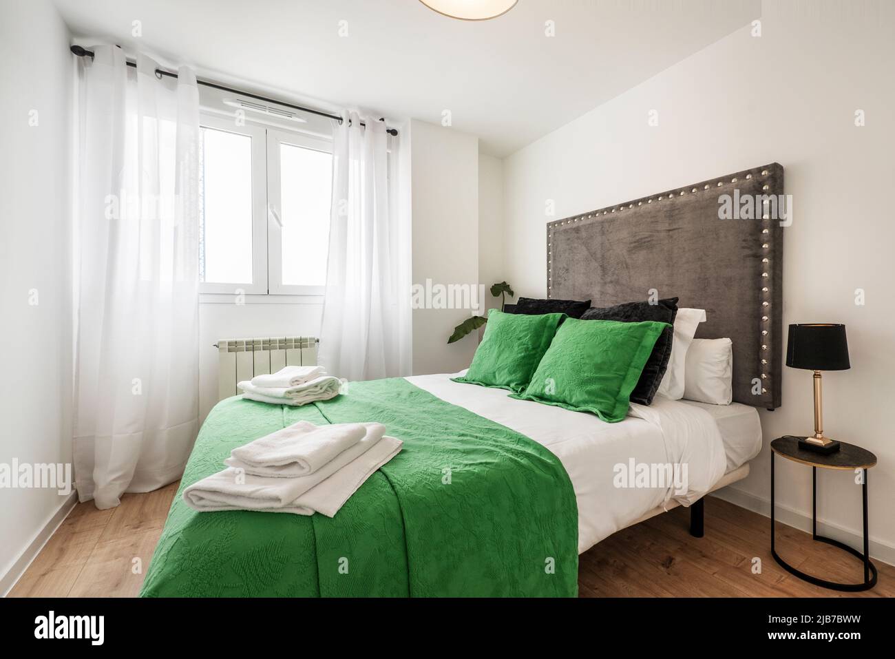 Chambre avec lit double, couvre-lit vert et coussins assortis, tête de lit  en tissu rembourré et rideaux blancs sur la fenêtre Photo Stock - Alamy