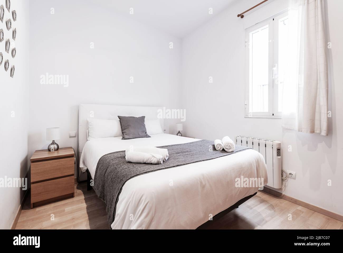 Chambre avec lit double, table de nuit en bois sombre avec tiroirs, fenêtre avec rideaux et couette blanche Banque D'Images