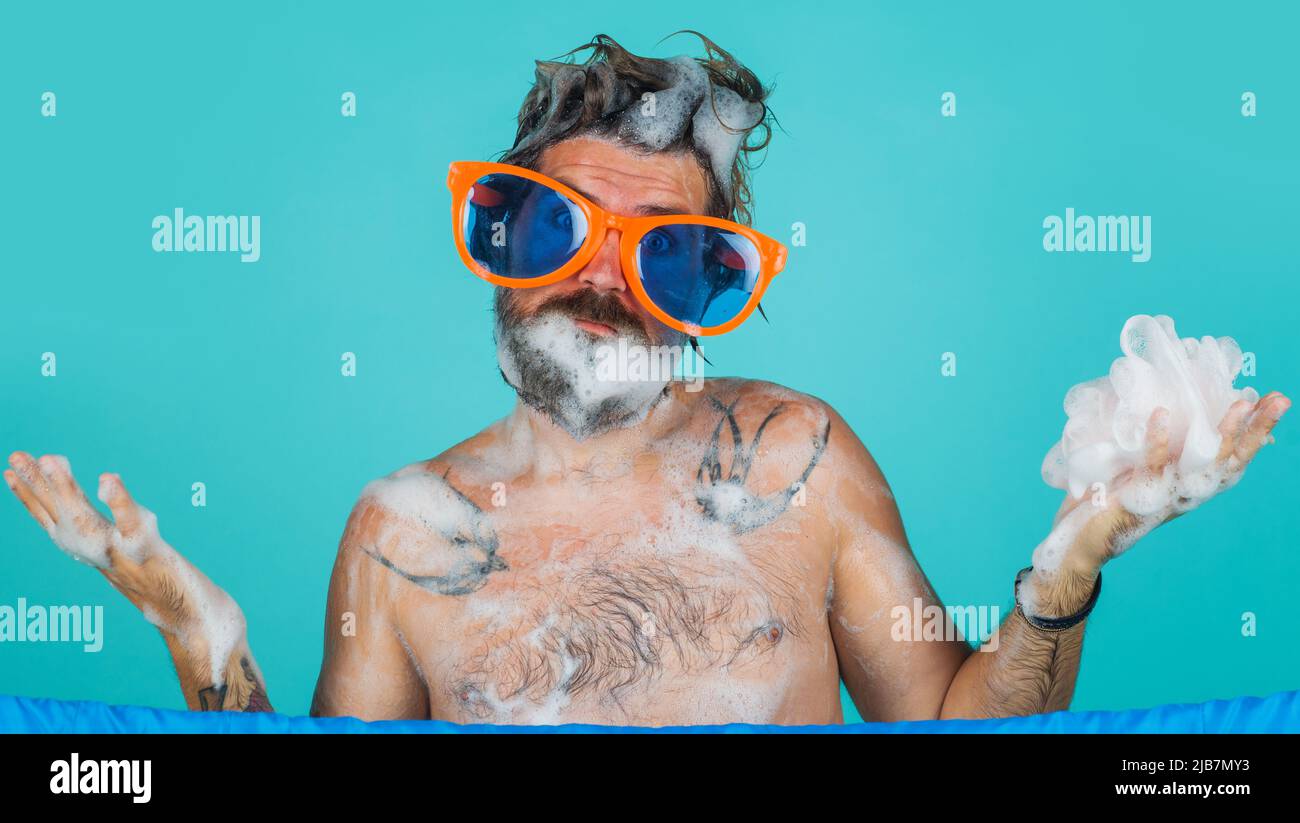 Homme barbu laver le corps avec du gel hydratant sous la douche. Un gars surprise dans de grands verres. Routine du matin. Banque D'Images