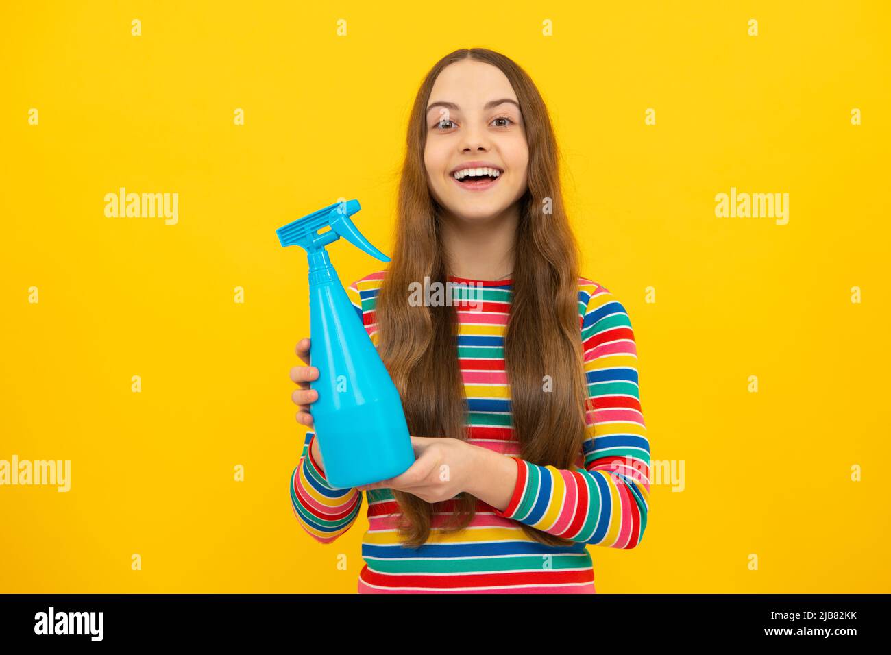 Jeune fille tenant une bouteille de détergent. Happy Kid Hold désinfectant produit en aérosol dans un flacon pour copier l'espace fond jaune, désinfection. Banque D'Images