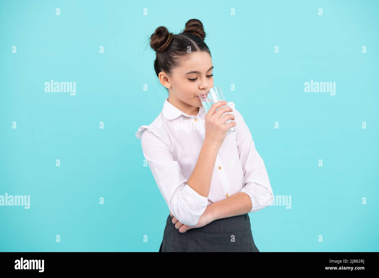 Une adolescente boit de l'eau à partir d'un verre isolé sur fond bleu. Vie quotidienne santé. Bonne adolescente, émotions positives et souriantes de la jeune fille. Banque D'Images
