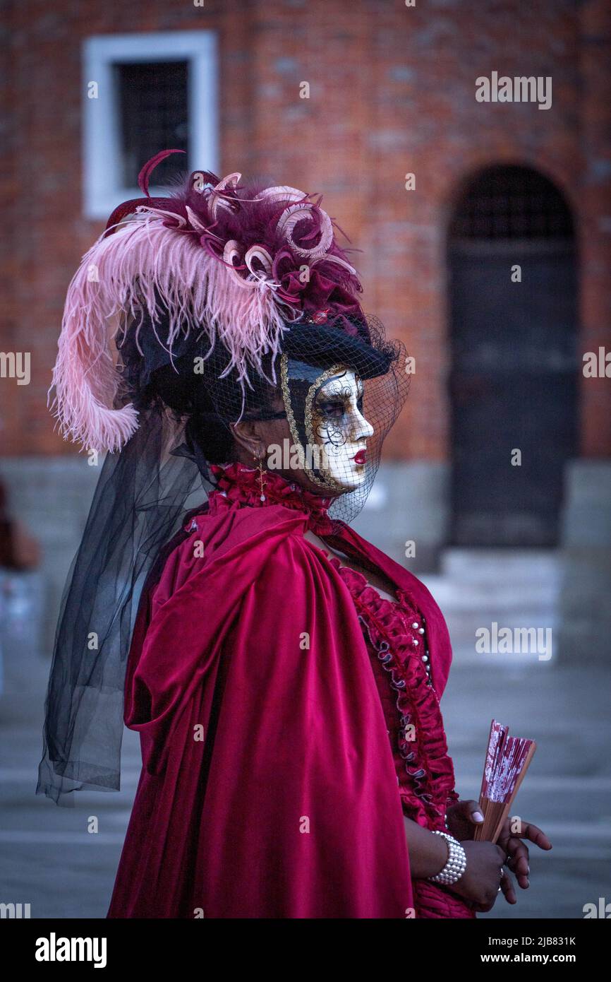 Venise, Italie - 18.02.2022: Femme masquée en robe rouge avec plumes roses et violettes au carnaval vénitien Banque D'Images