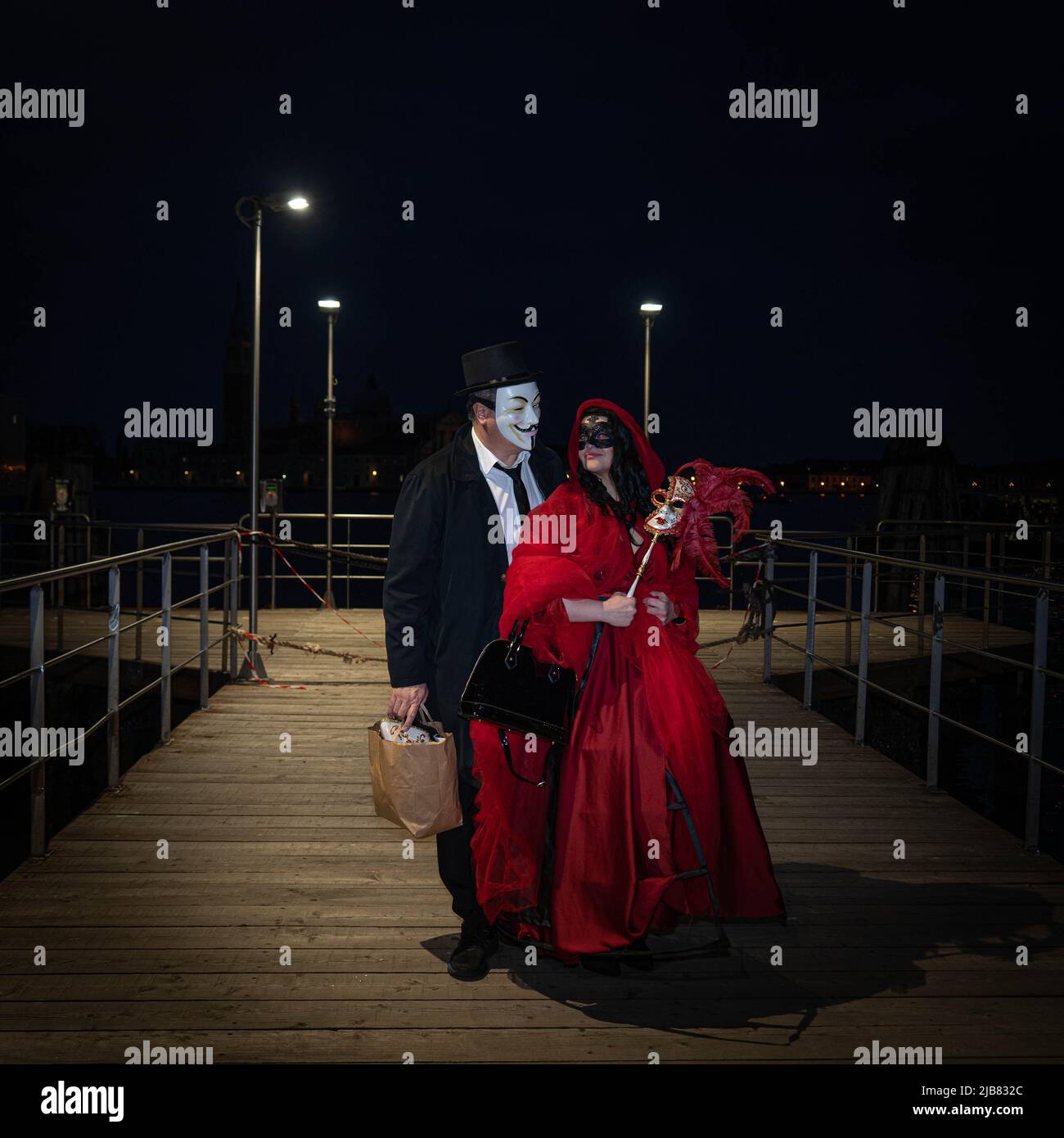 Venise, Italie - 18.02.2022: Un homme et une femme en costumes de carnaval vénitien debout sur une jetée en bois au Grand Canal, Venise la nuit Banque D'Images