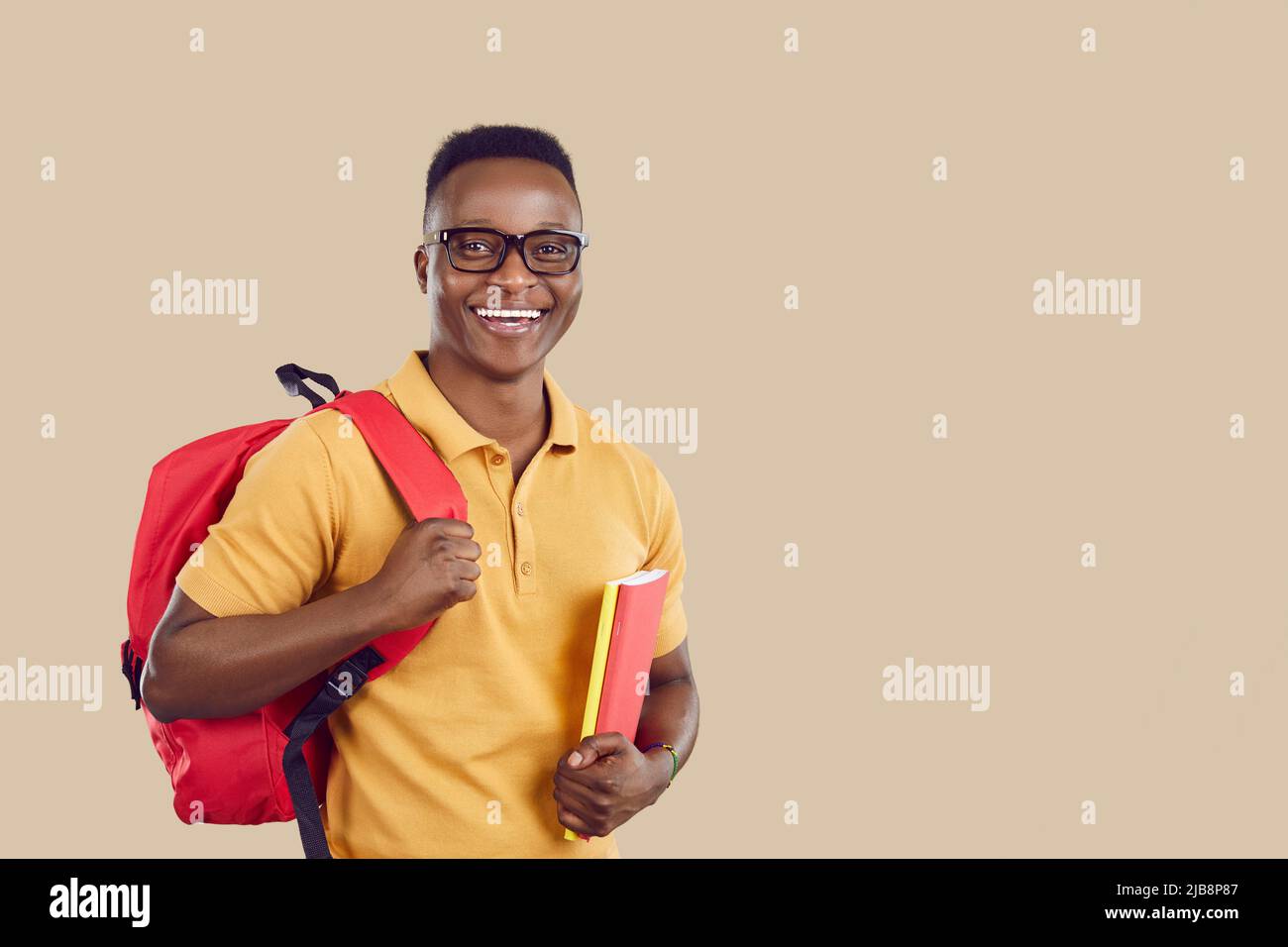 Joyeux étudiant afro-américain avec sac et livres debout sur fond beige copie espace Banque D'Images