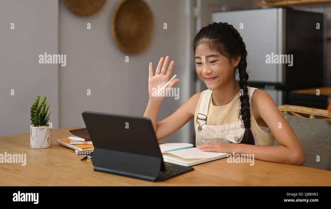 Fille asiatique souriante ayant cours en ligne sur tablette d'ordinateur tout en étant assis à la table de cuisine. Concept de l'éducation virtuelle, homeschooling Banque D'Images