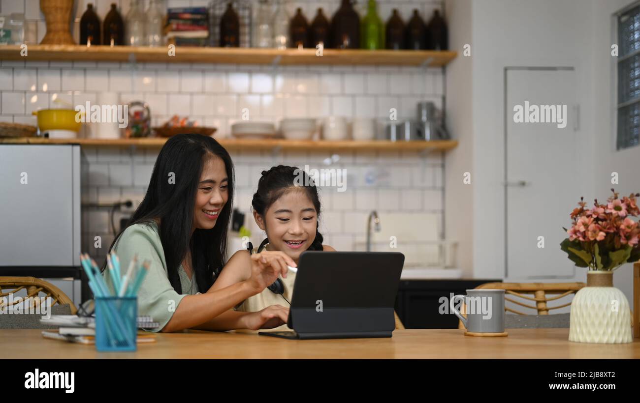 Maman asiatique aidant sa petite fille à faire ses devoirs tout en s'assis à la cuisine maison Banque D'Images