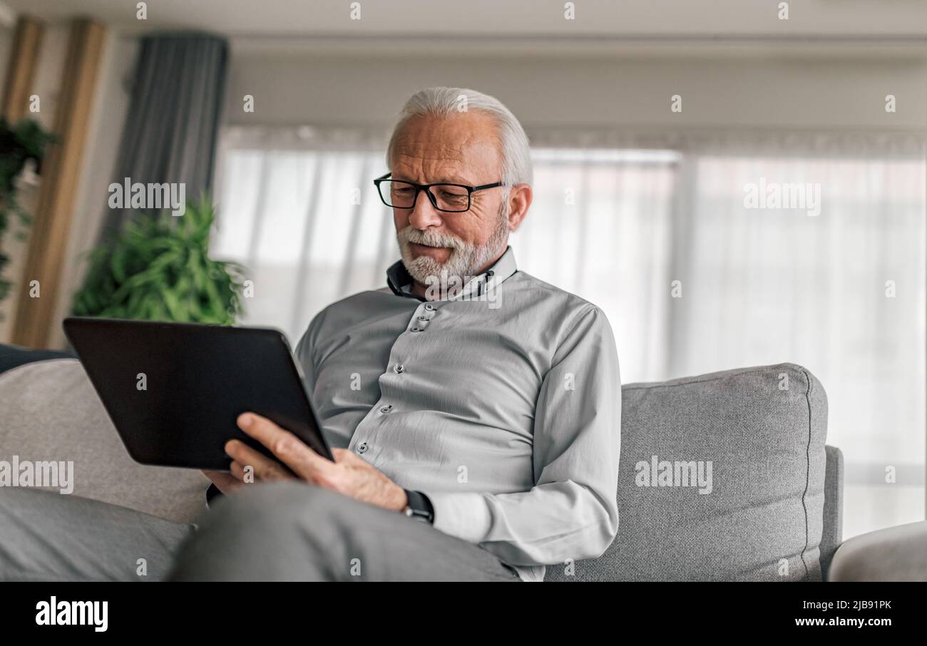 Homme d'affaires expérimenté confiant utilisant une tablette numérique. Les hommes âgés professionnels portent des formes. Il utilise un ordinateur sans fil lorsqu'il se repose sur le canapé A. Banque D'Images
