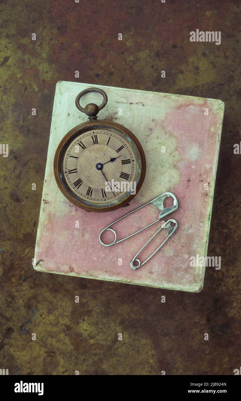 Montre de poche antique reposant sur une boîte en carton rose éraflée avec deux épingles de sécurité Banque D'Images