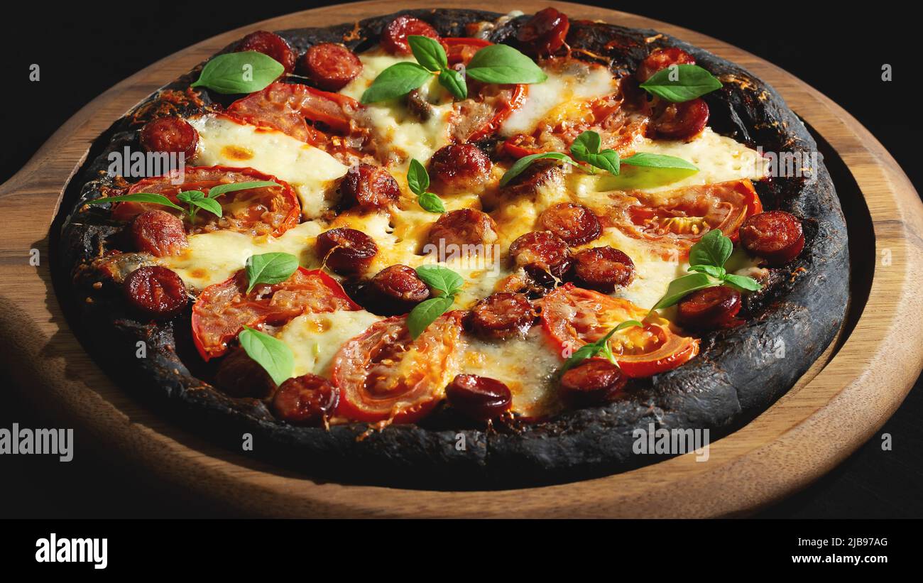 Pizza noire avec tomates, saucisses, mozzarella et basilic. Pâte à base de poudre de charbon de bambou saine Banque D'Images