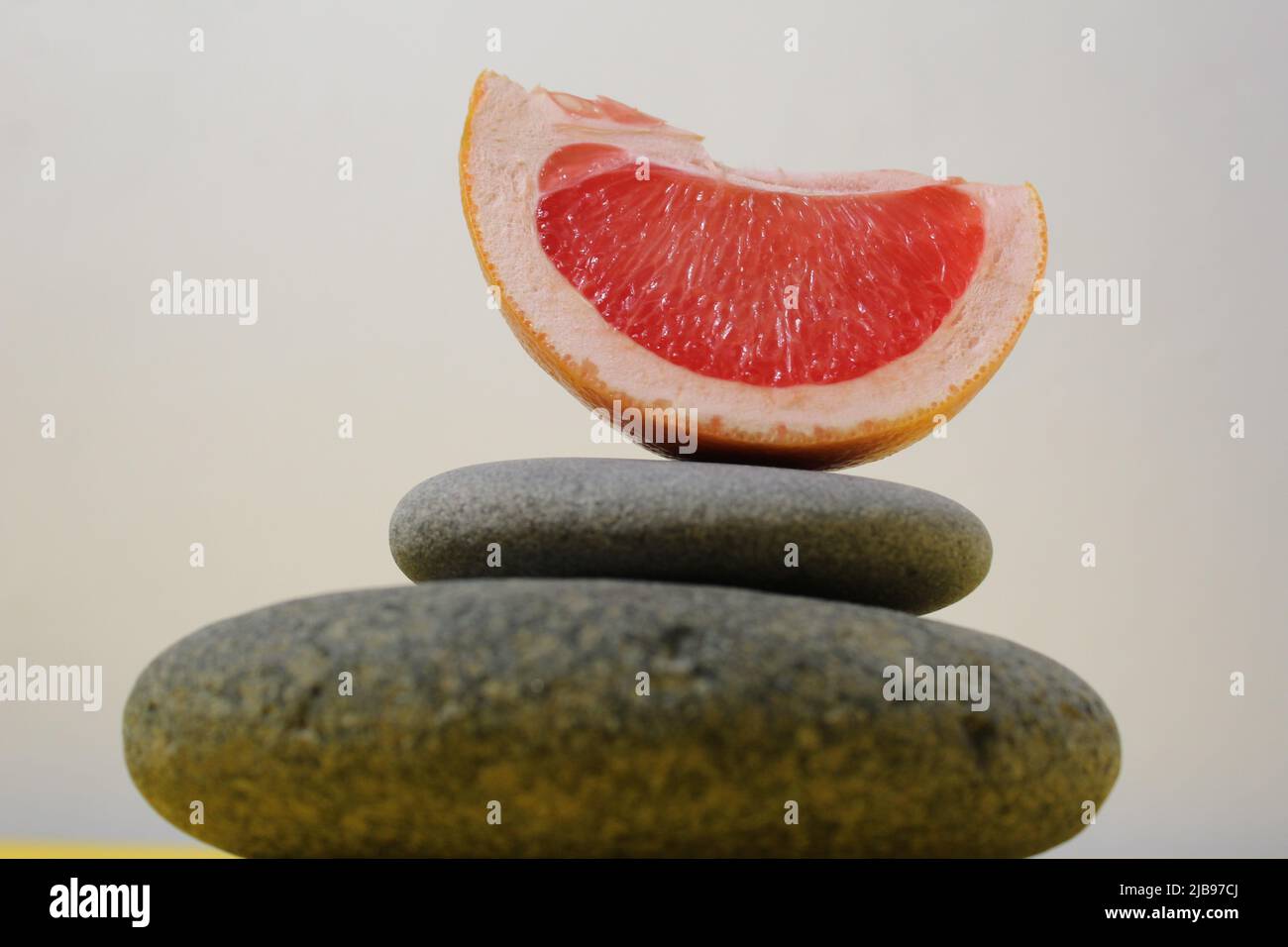 une tour de balans de pierres grises et de fruits orange de pamplemousse sur fond blanc jaune avec de la place pour le texte. Avantages de l'énergie importance de la santé Vitami Banque D'Images