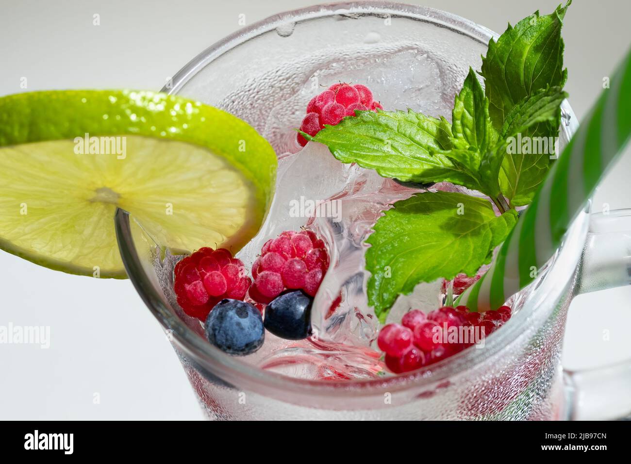Cocktail d'été rafraîchissant avec glace, citron vert et baies dans un verre avec paille Banque D'Images