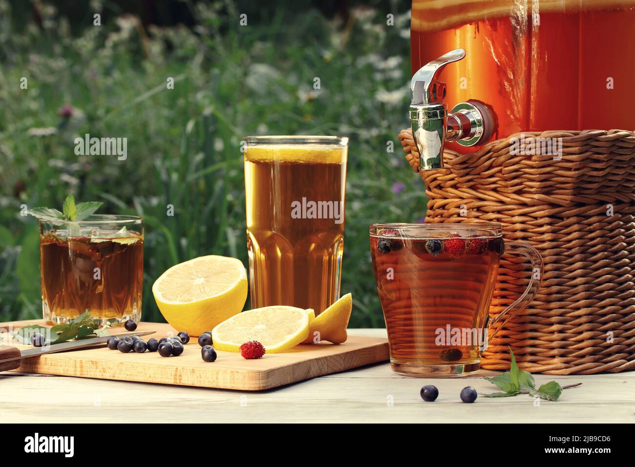 Une boisson faite maison au kombucha aux champignons dans un pot avec robinet et dans des verres avec menthe, baies et citron sur une table en bois. Banque D'Images