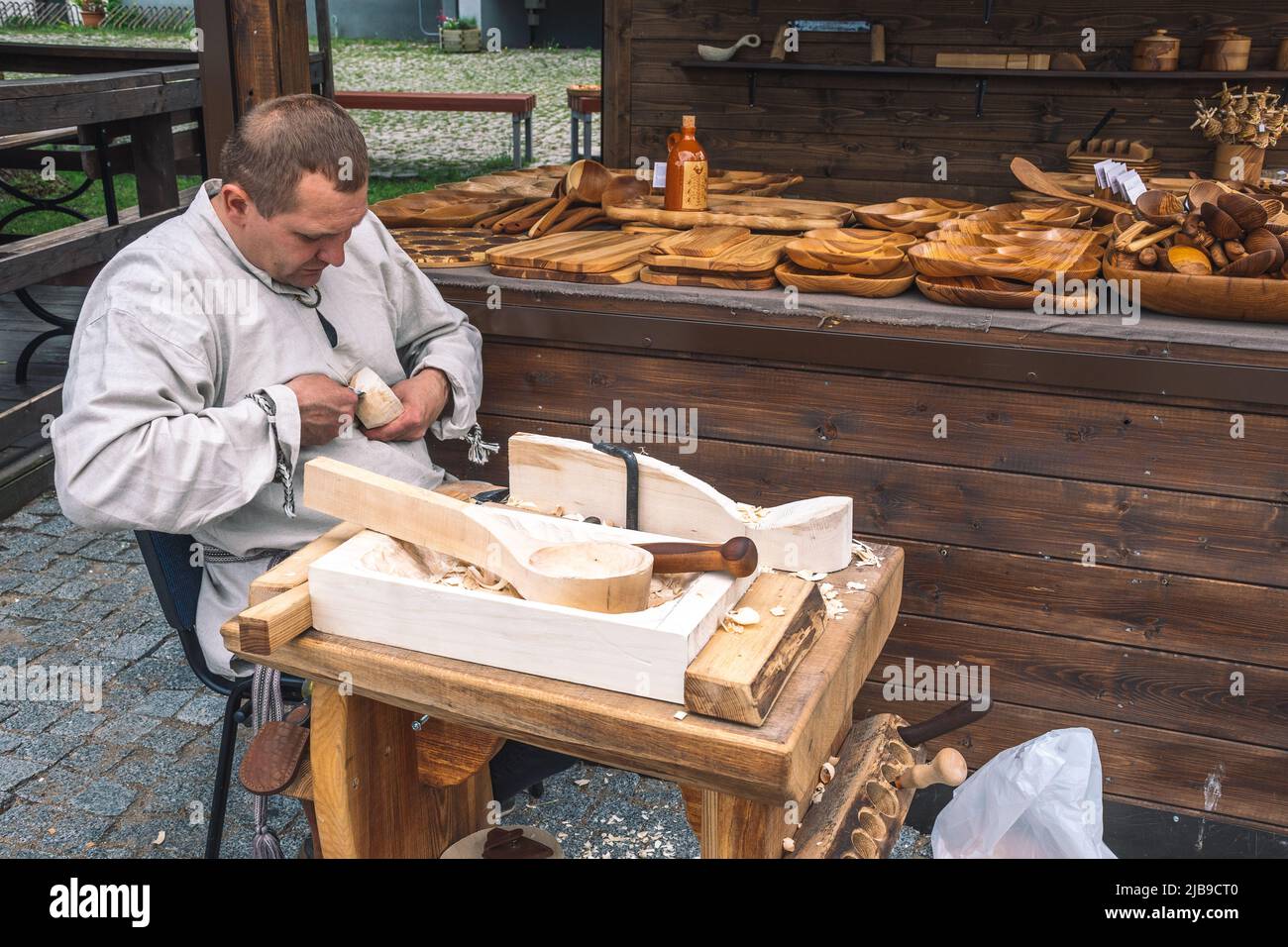 Un artisan lituanien en costumes traditionnels sculptant une coupe de bois et vendant ses objets et objets en bois faits main sur un marché de rue local Banque D'Images