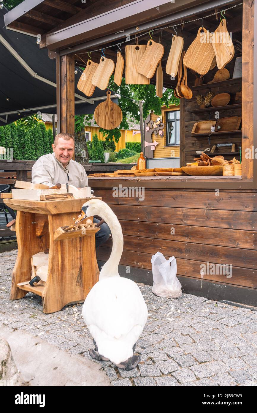 Un artisan lituanien en costumes traditionnels sculptant du bois et vendant ses objets et objets en bois faits main sur un marché de rue local à Trakai Banque D'Images