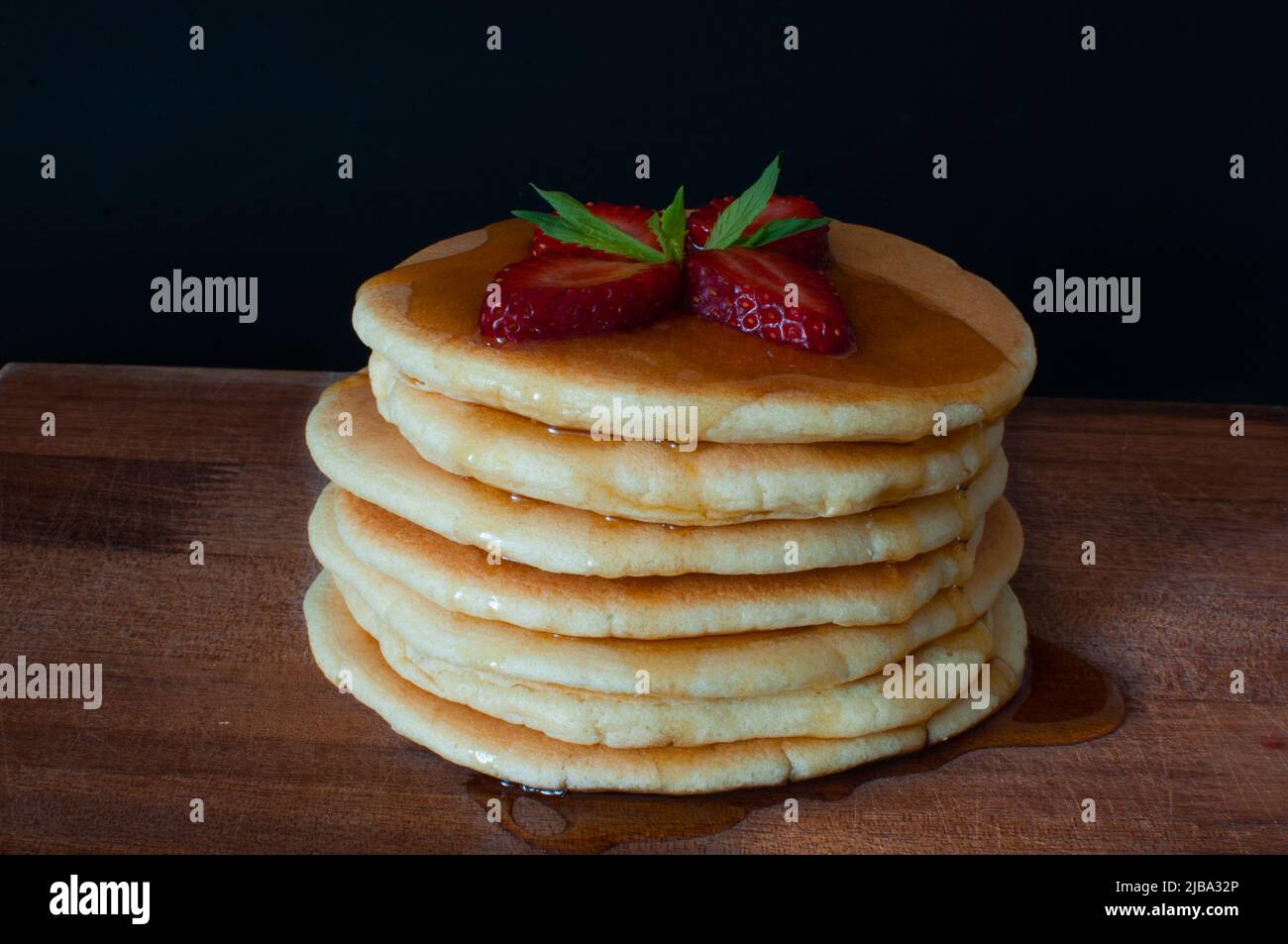 Crêpes aux fraises fraîches, à la menthe et au sirop sur une assiette en bois. Isolé sur fond sombre, concentré sélectif, en-cas de petit-déjeuner américain. Banque D'Images