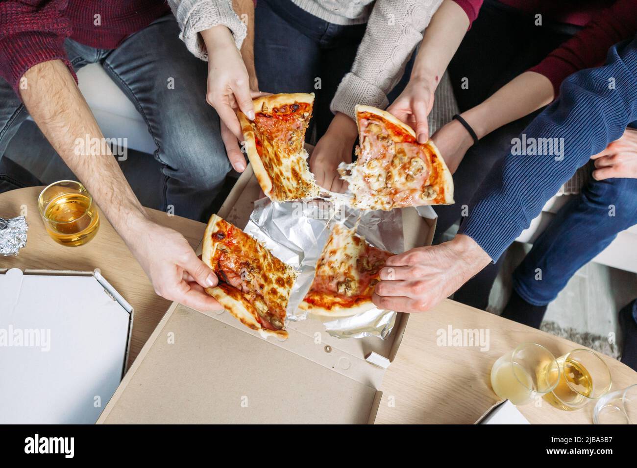 Les mains des hommes et des femmes attrapant des morceaux de pizza. Soirée cinéma à la maison avec des amis Banque D'Images