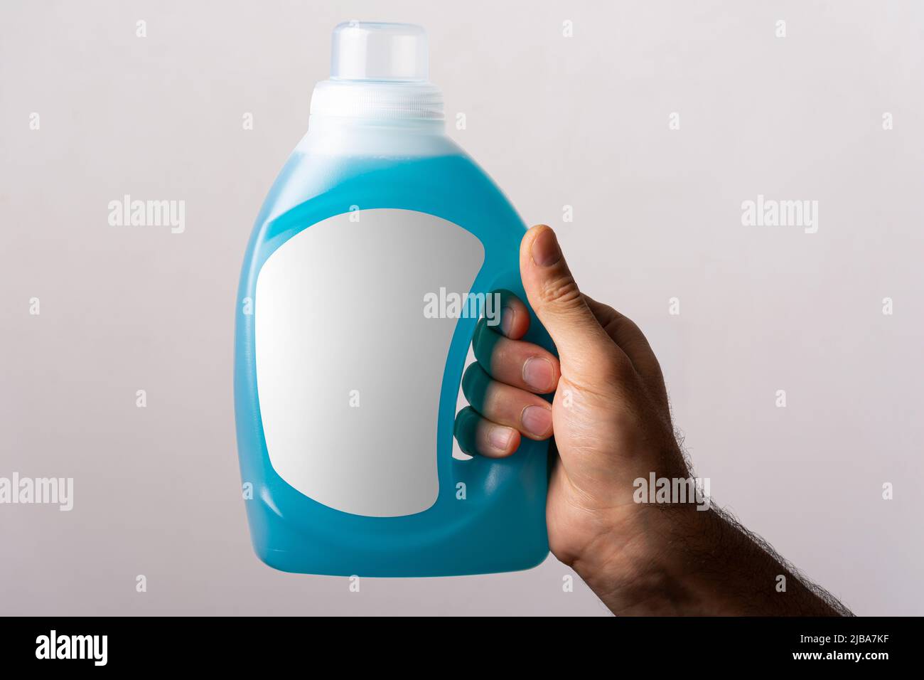 Main mâle tenant une bouteille de détergent liquide en tissu, modèle de série maquette modifiable prêt à l'emploi, chemin de sélection d'étiquette de bouteille inclus. Banque D'Images