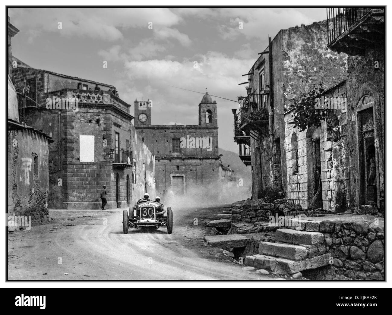 Vintage 1930 Targa Florio avec le vainqueur Achille Varzi dans son Alfa Romeo P2 passant par un village rural sicilien. Le Targa Florio 1930 était une course automobile de Grand Prix qui n'avait pas de championnat et qui s'est déroulée sur un parcours de 108 km (67 miles) composé de routes publiques sur l'île italienne montagneuse de Sicile. Banque D'Images