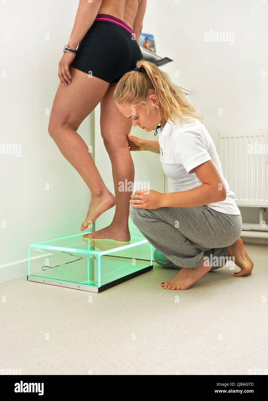 Une jeune physiothérapeute femme diagnostique sa patiente sur une analyse du pas du pied. Le voyant vert indique les empreintes sur le panneau du scanner Banque D'Images